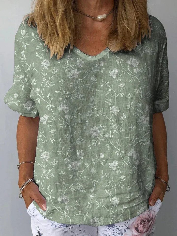 Woman wearing sage green floral short sleeve blouse with white pants featuring pink rose print