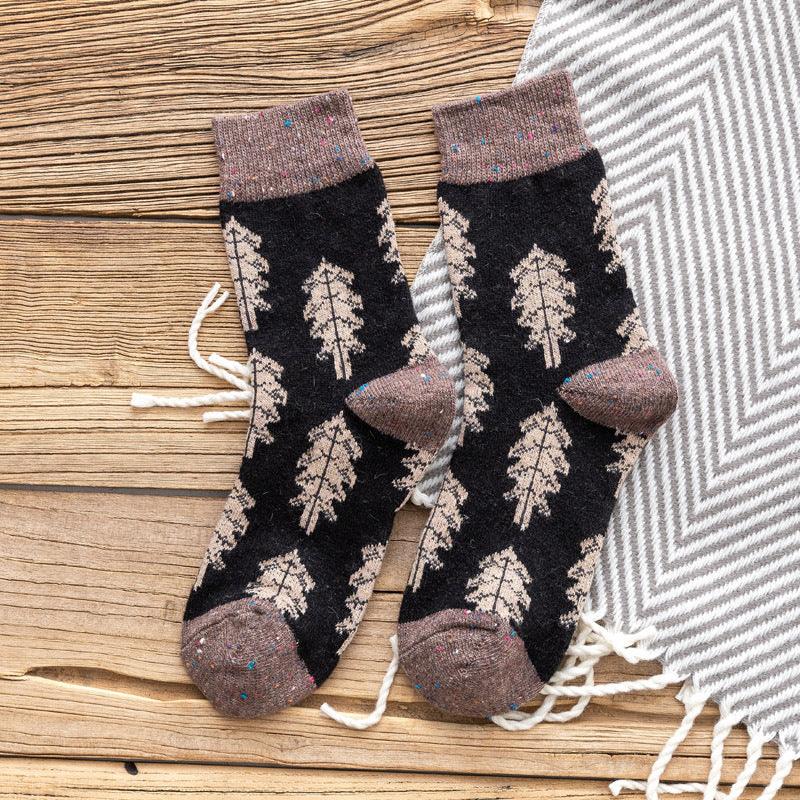 Black and brown wool socks with leaf patterns on a wooden surface next to a white and gray fringed blanket