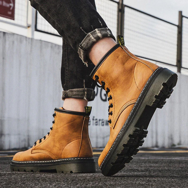 Tan leather lace-up rugged boots worn with rolled black jeans on asphalt urban street