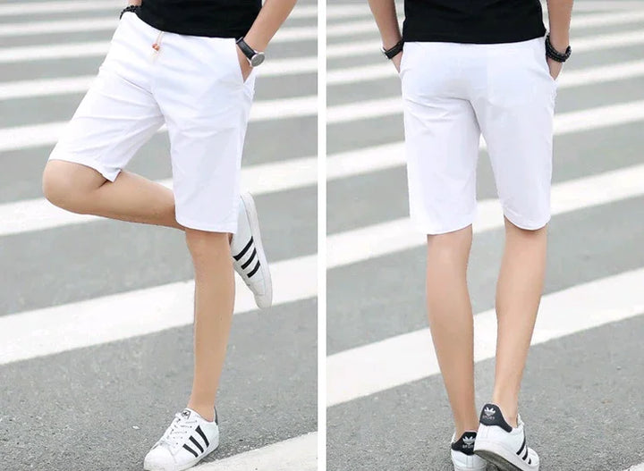 Man wearing white casual shorts and black sneakers standing on a pedestrian crossing outdoors