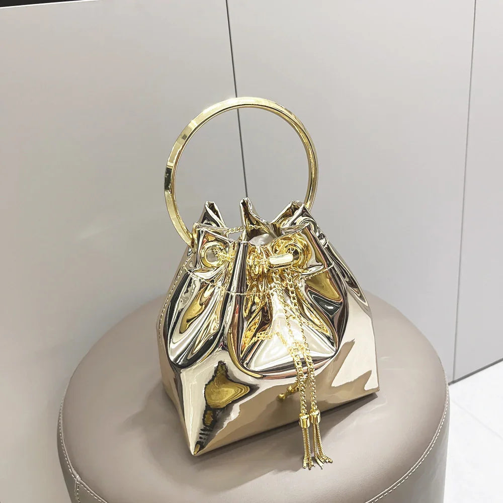 Shiny metallic gold handbag with round handle and drawstring detail on beige stool