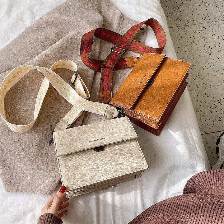 Two stylish leather crossbody bags, one beige with cream strap, one brown with red strap, on bed with beige blanket