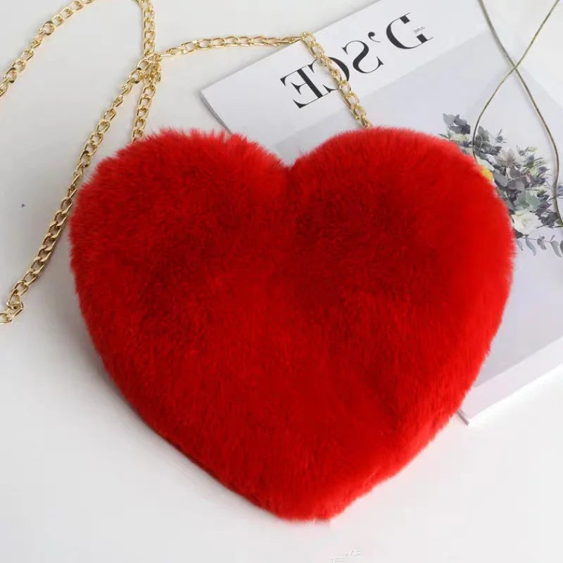 Red fluffy heart-shaped handbag with gold chain strap on white surface with magazine
