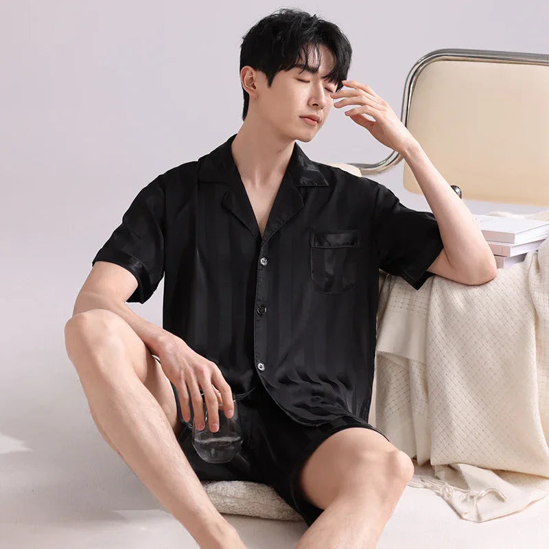 Man wearing black satin striped short sleeve pajama set sitting relaxed holding glass