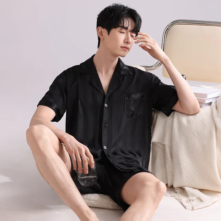 Man wearing black satin striped short sleeve pajama set sitting relaxed holding glass