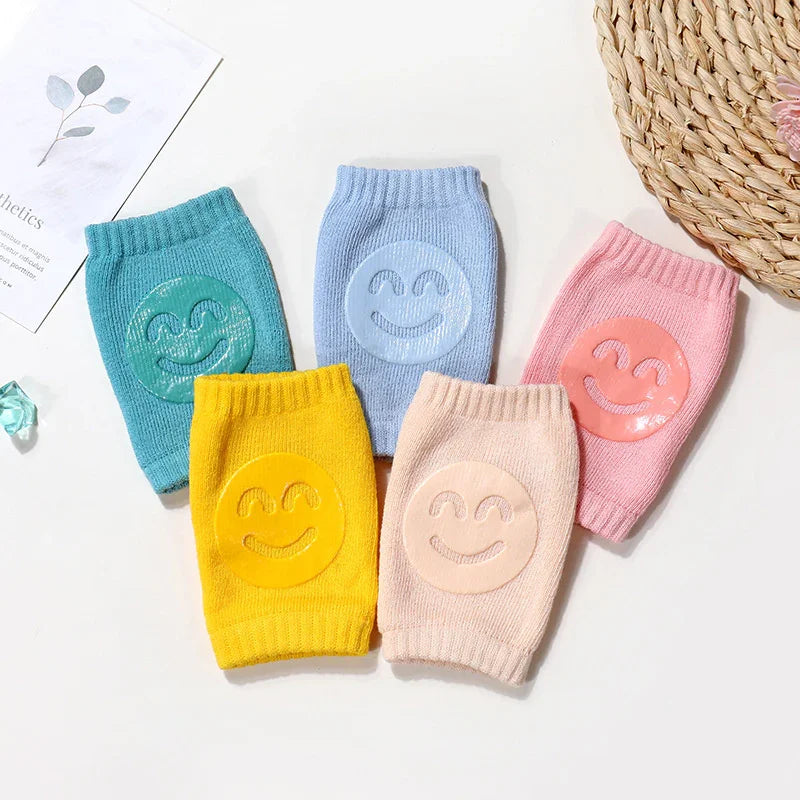 Colorful knitted wrist warmers with smiling emoji patches in yellow, blue, pink, and green on a white surface
