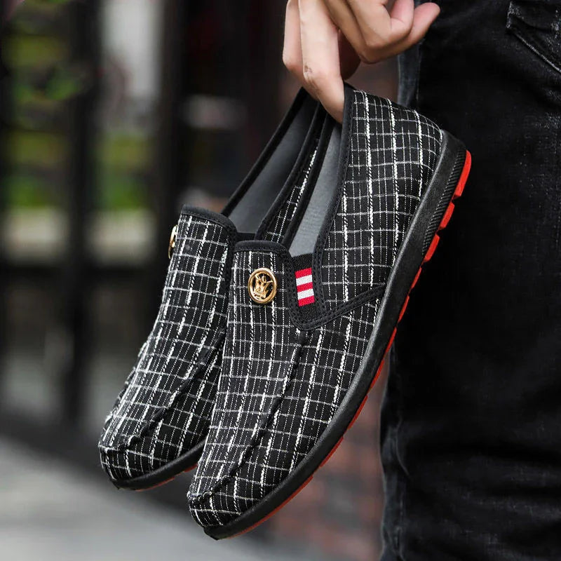 Black and white checkered slip-on shoes with red stripe detail and gold emblem, held by hand