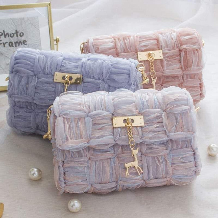 Three pastel-colored woven handbags with gold deer charm, in lilac, pink, and lavender shades on a white surface
