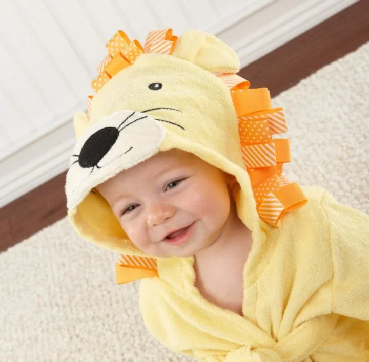 Smiling baby wearing a yellow lion-themed hooded towel with orange ribbon mane sitting on carpet