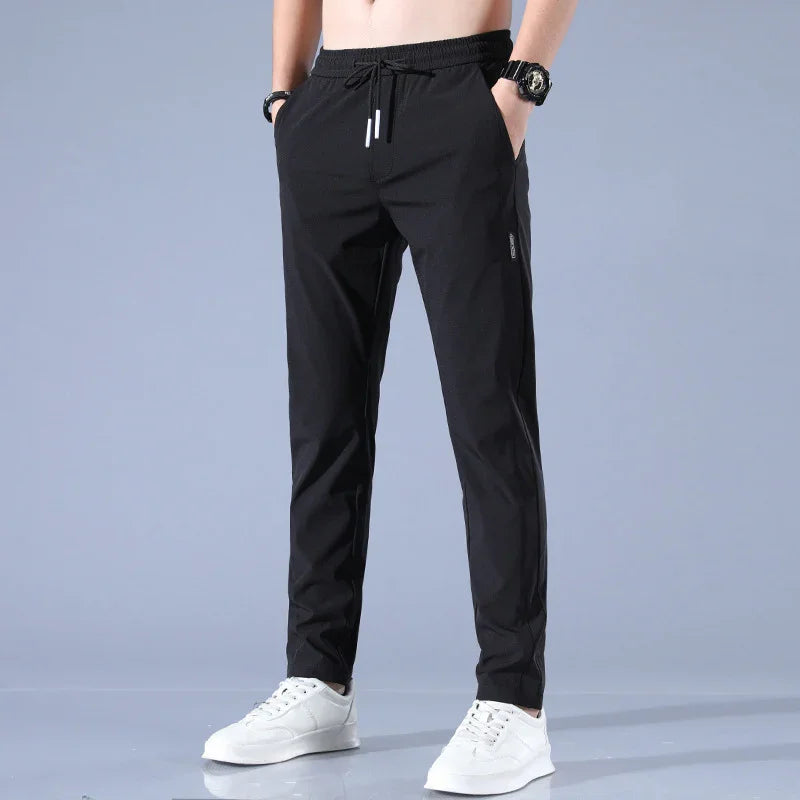 Men's black casual drawstring pants with pockets, paired with white sneakers and wristwatch