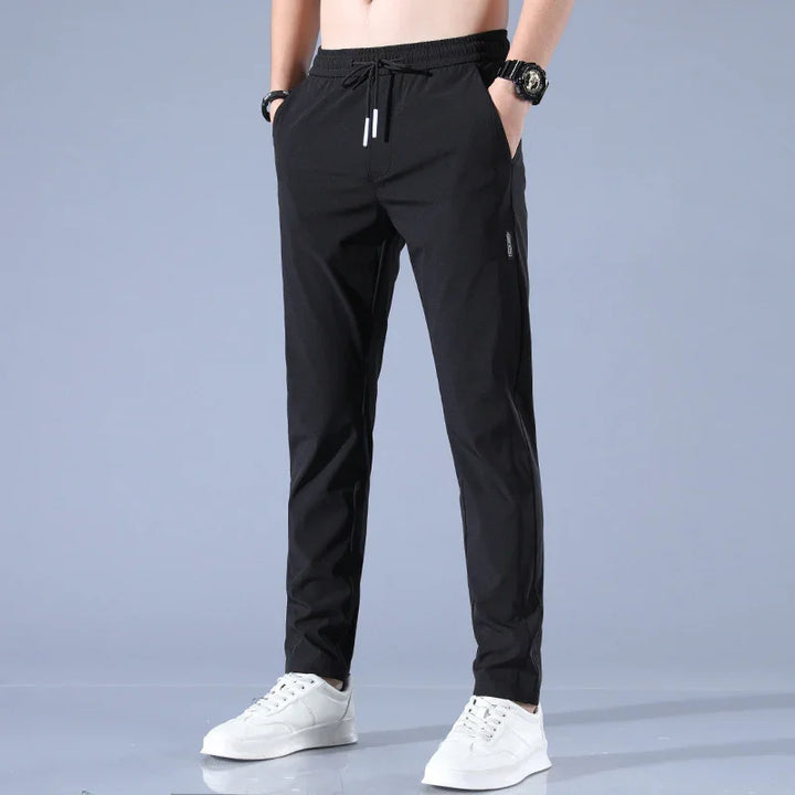 Men's black casual drawstring pants with pockets, paired with white sneakers and wristwatch