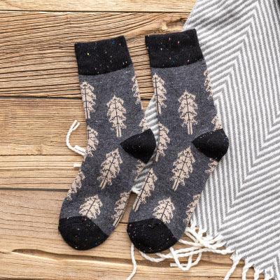 Cozy gray wool socks with black cuffs and beige tree pattern on wooden floor next to a gray striped blanket