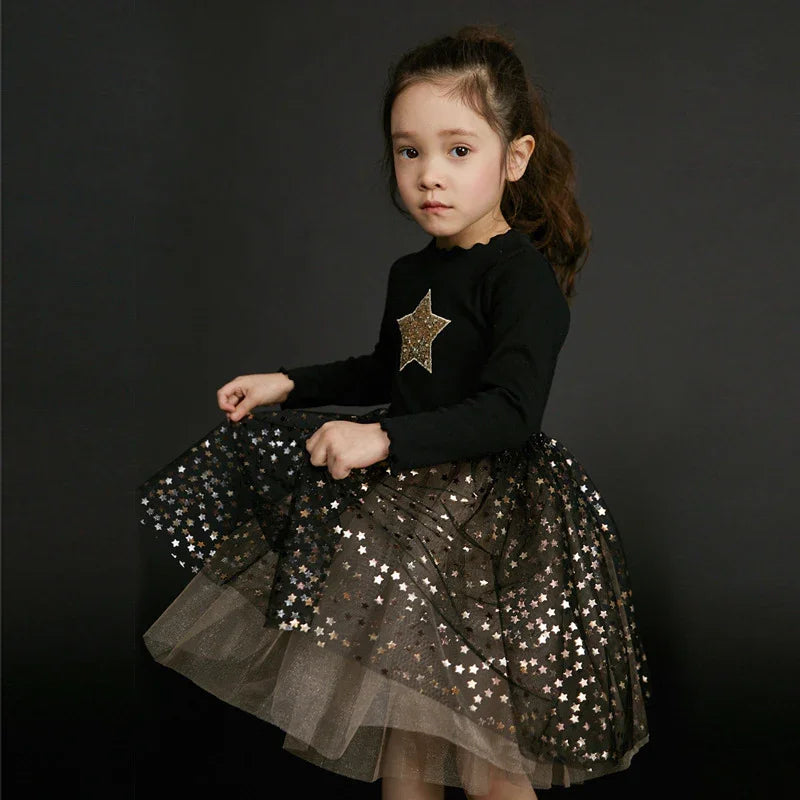 Young girl wearing black dress with gold star design and star-patterned tulle skirt on dark background