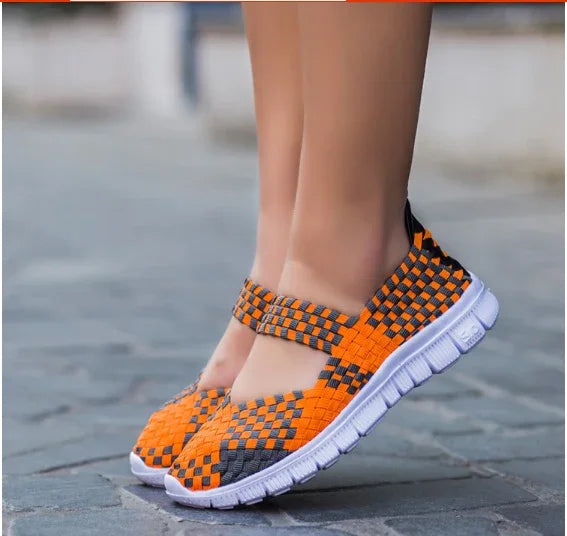 Close-up of orange and black woven slip-on shoes with white flexible soles on pavement