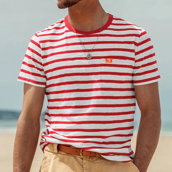 Man wearing red and white striped t-shirt with necklace and beige pants on a beach