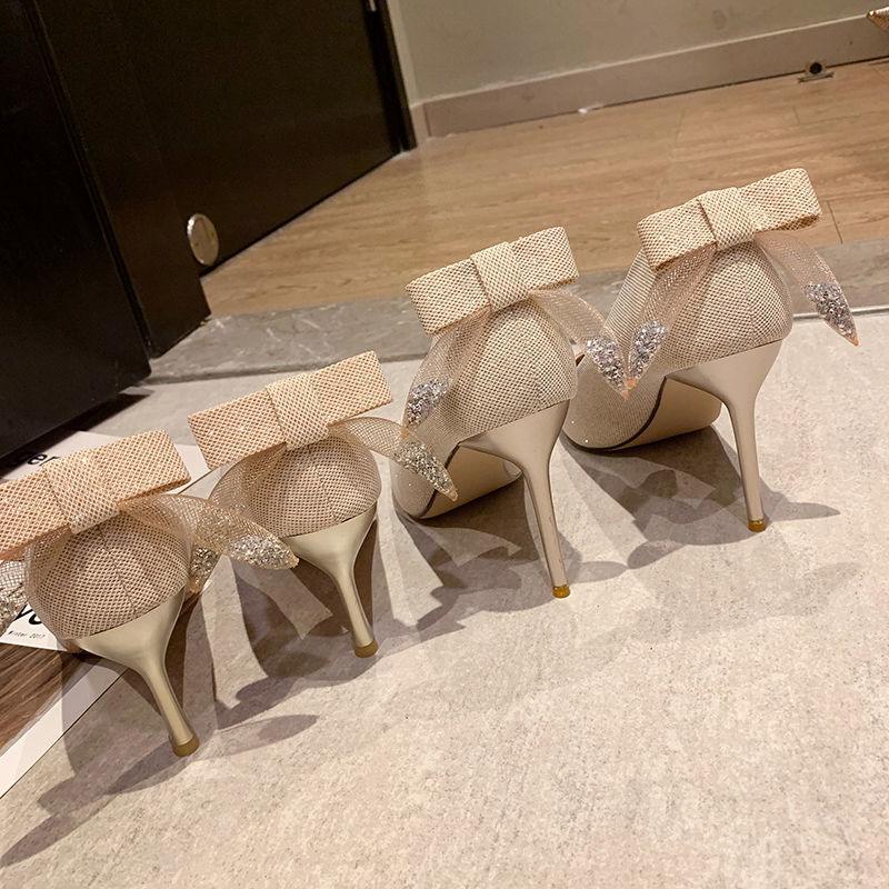 Pair of beige high heel shoes with mesh bows and glitter accents on wooden and tiled floor