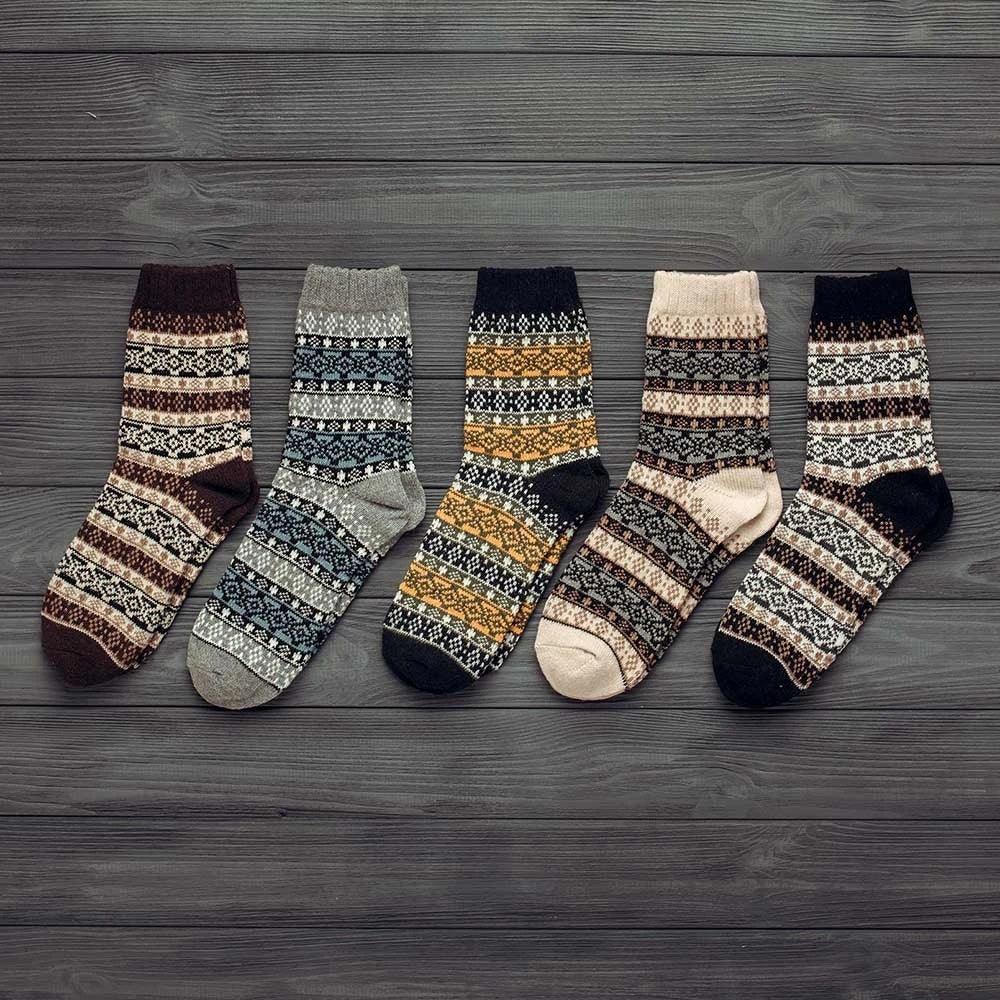 Five pairs of cozy patterned wool winter socks in various colors on dark wooden background
