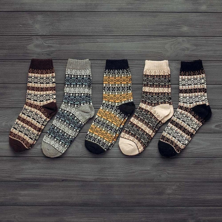 Five pairs of cozy patterned wool winter socks in various colors on dark wooden background