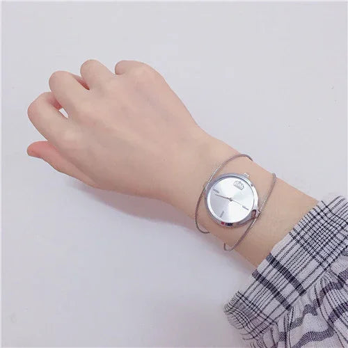 Minimalist silver wristwatch with mesh band on a wrist wearing plaid sleeve