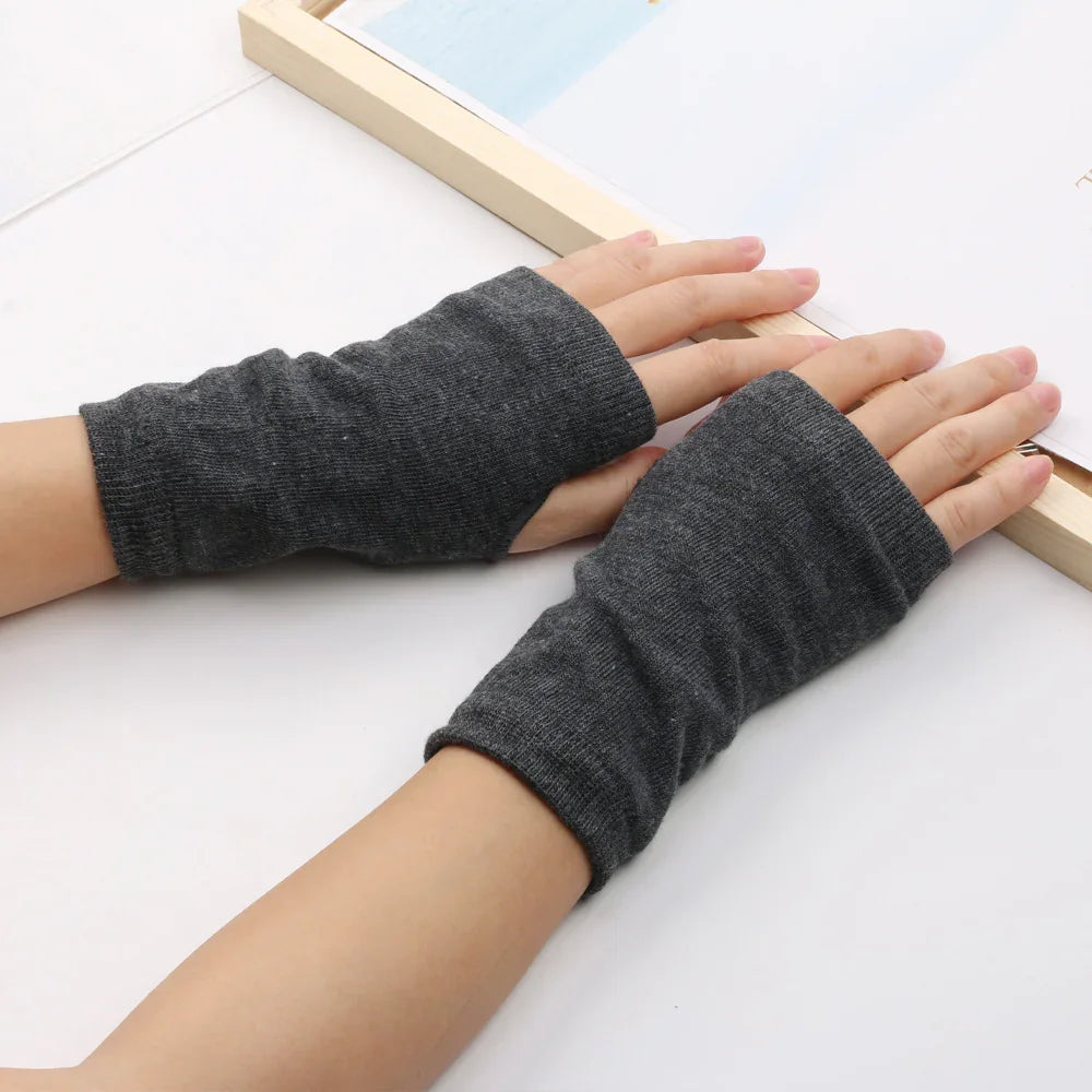 Hands wearing dark gray fingerless knit gloves on a white surface near a wooden picture frame