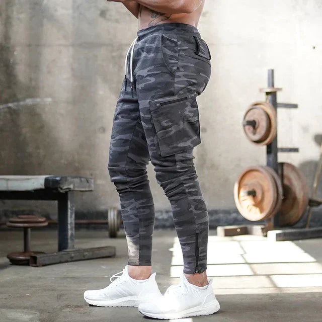 Man wearing gray camo cargo jogger pants and white sneakers in a gym with weightlifting equipment
