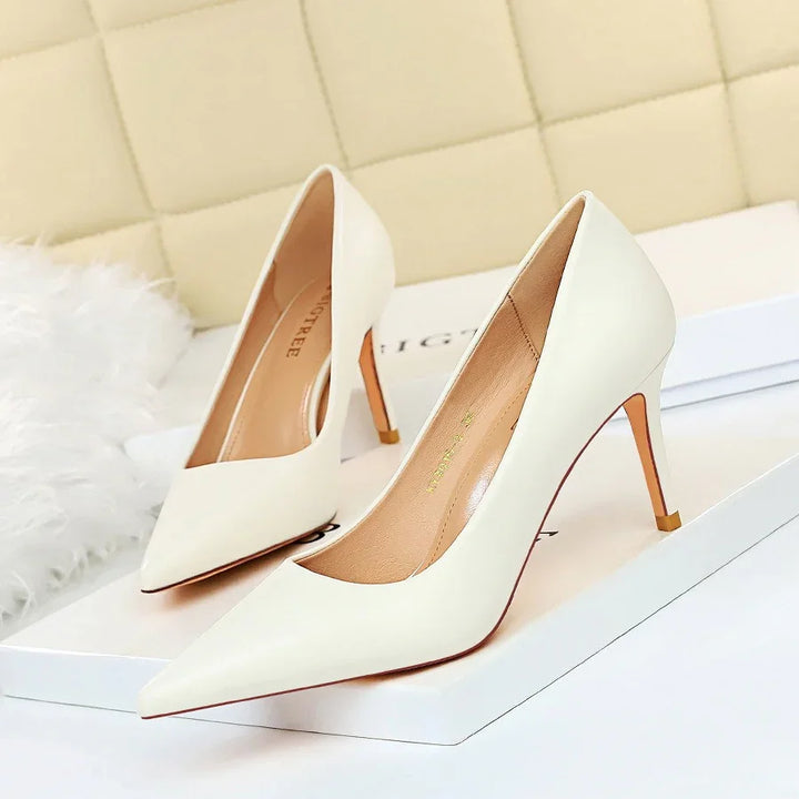 Pair of elegant white pointed-toe high heel pumps on a white box with beige cushioned background