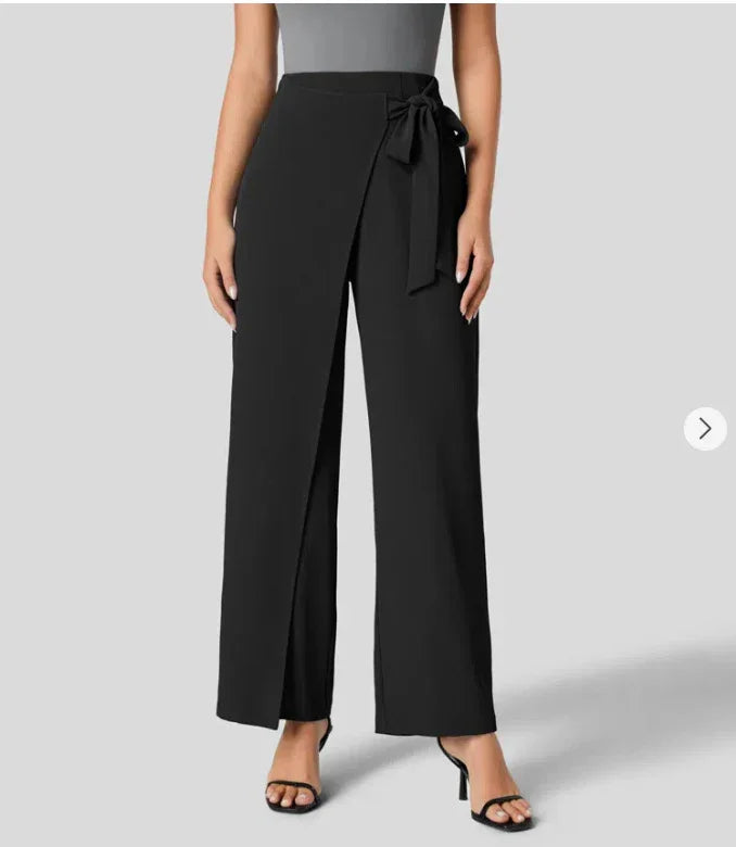Woman wearing black high-waist wide-leg pants with front wrap and bow detail, paired with black sandals