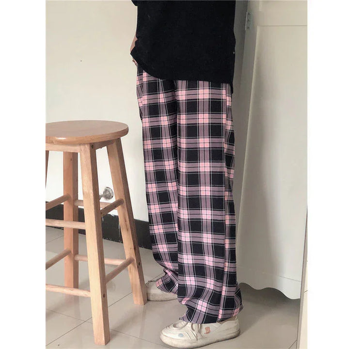 Person wearing pink and black plaid pants with white sneakers standing next to a wooden stool indoors