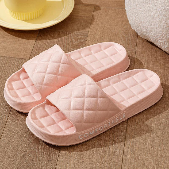 Pair of pink cushioned indoor slide slippers with quilted design on wood floor