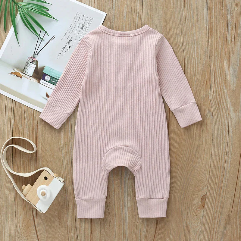 Soft pink ribbed long-sleeve baby romper on wooden surface with toy camera and leaves