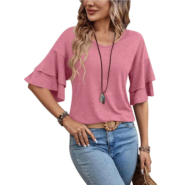 Woman wearing pink ruffle sleeve blouse with V-neck and blue jeans holding woven bag