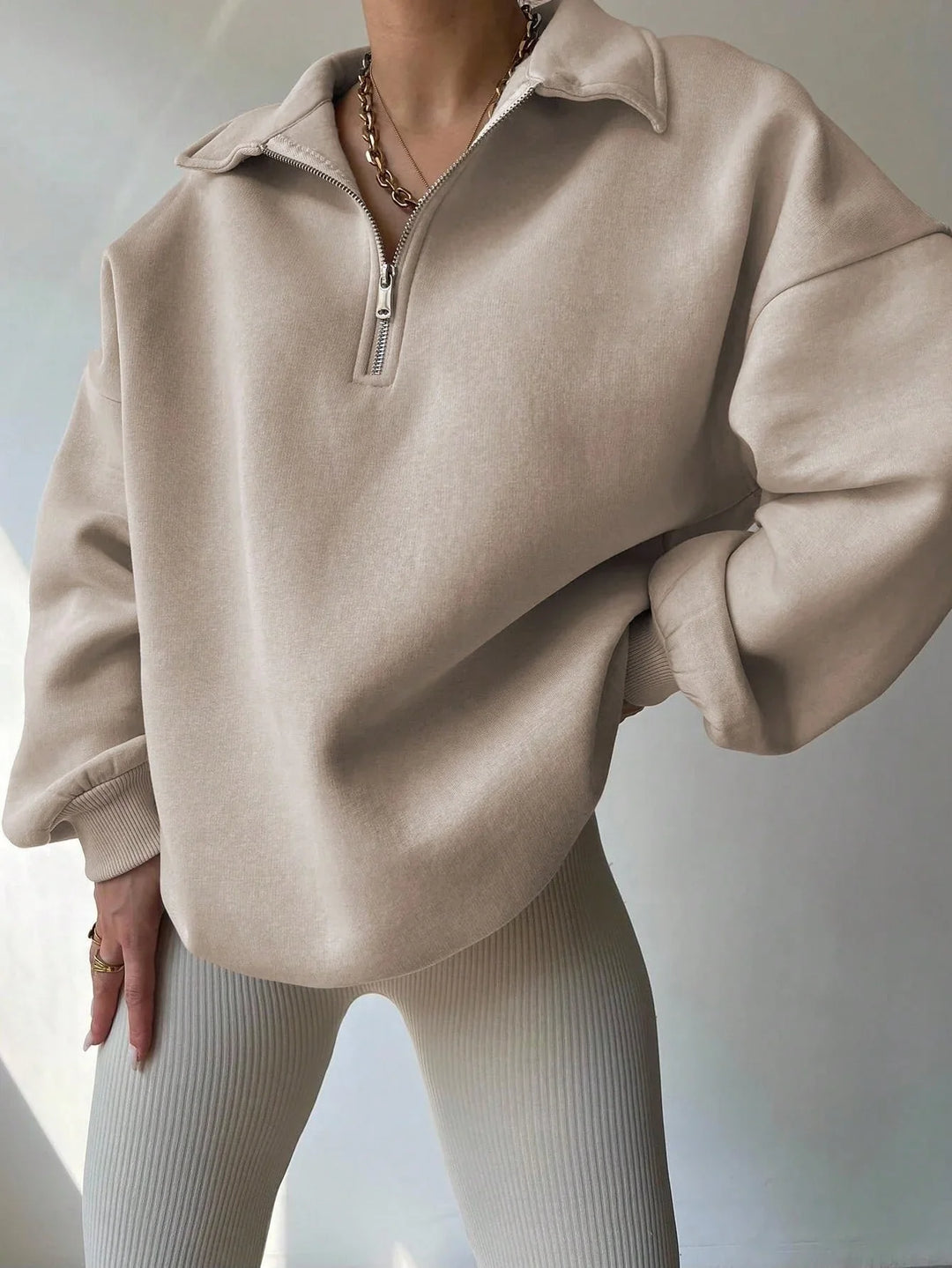 Person wearing beige half-zip sweatshirt and ribbed knit leggings with gold chain necklace