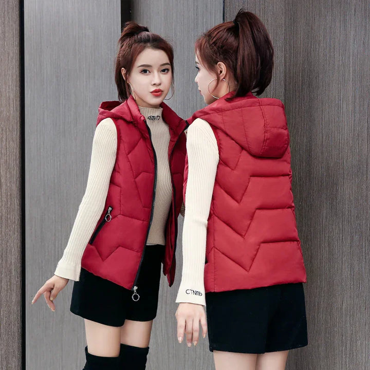Woman wearing a red quilted hooded vest over a beige ribbed sweater and black skirt, posing in front of a mirror