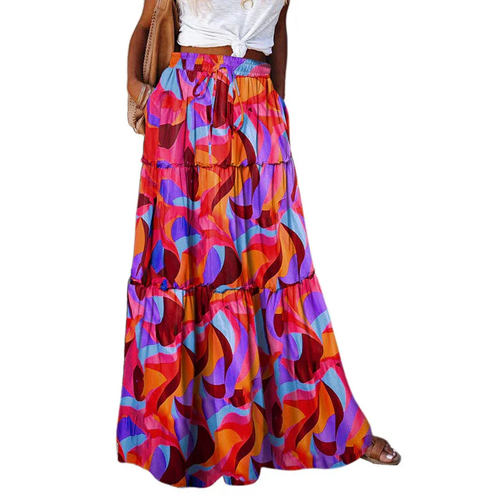 Woman wearing a colorful abstract patterned maxi skirt with a white knotted top and brown bag