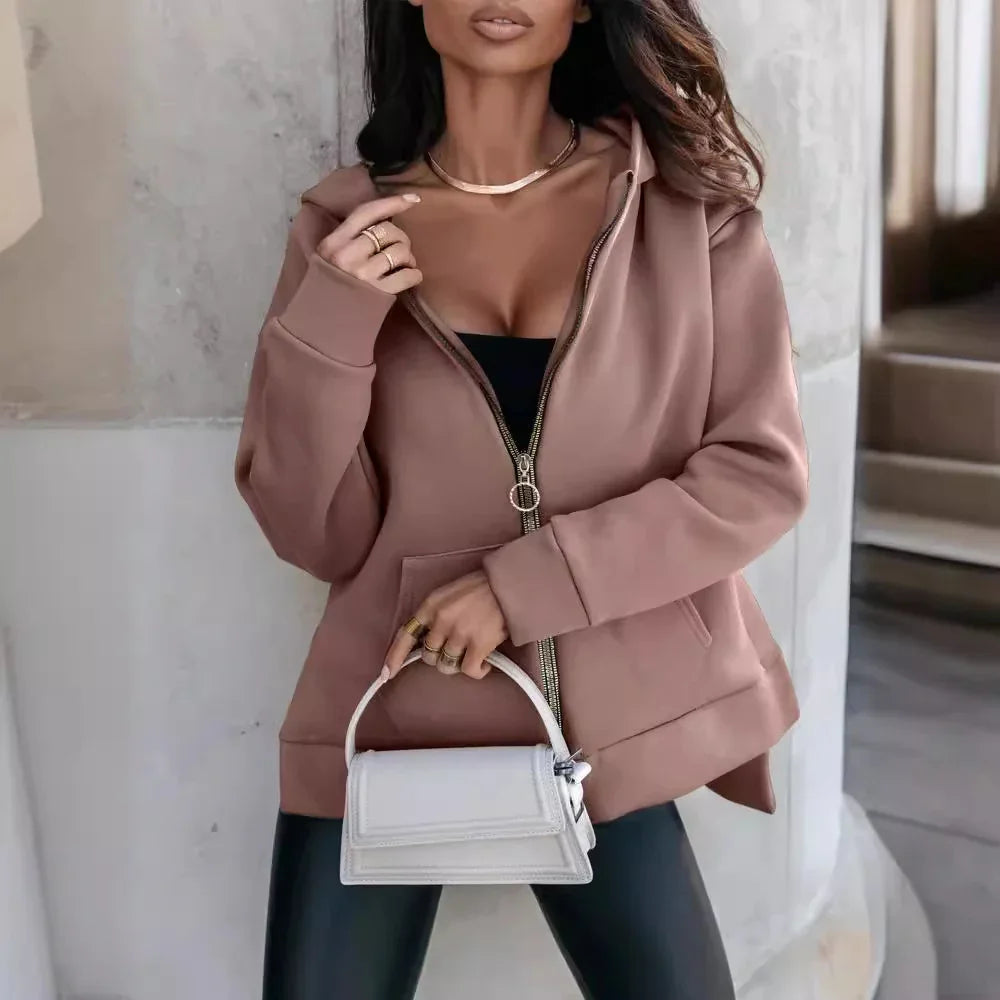 Woman wearing brown zip-up hoodie and black top holding a white handbag indoors