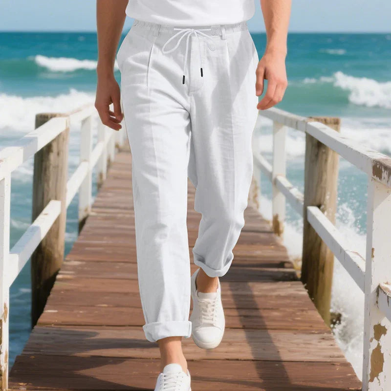 Person wearing white drawstring pants and sneakers walking on wooden pier by ocean