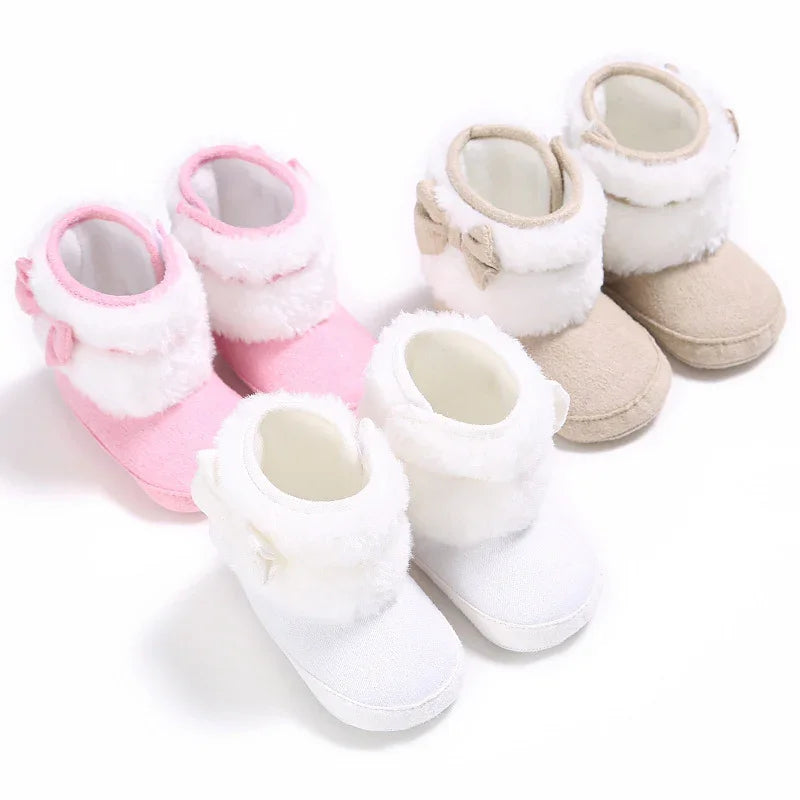 Three pairs of soft baby boots in pink, white, and beige with fluffy white trim and bows