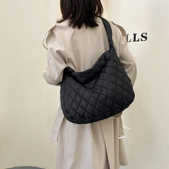 Woman wearing beige trench coat carrying a black quilted shoulder bag indoors