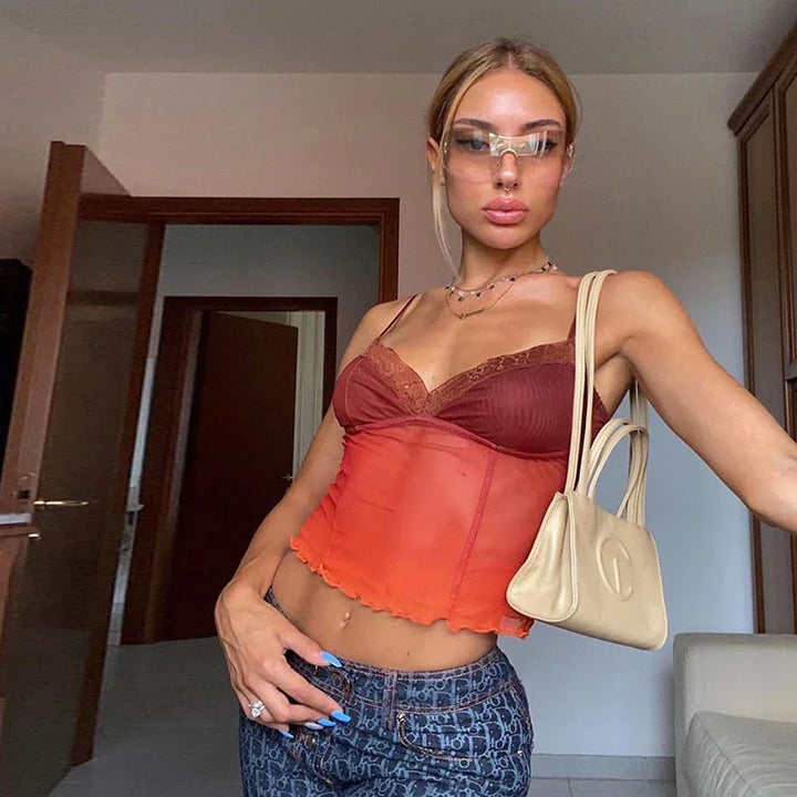 Young woman wearing orange sheer top, designer jeans, clear futuristic sunglasses, and beige handbag in modern room