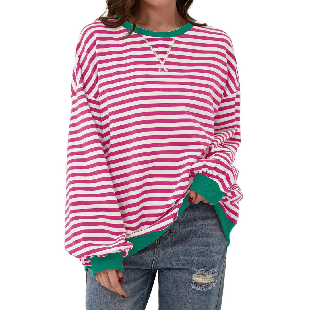 Woman wearing oversized pink and white striped sweater with green cuffs and collar, paired with ripped blue jeans