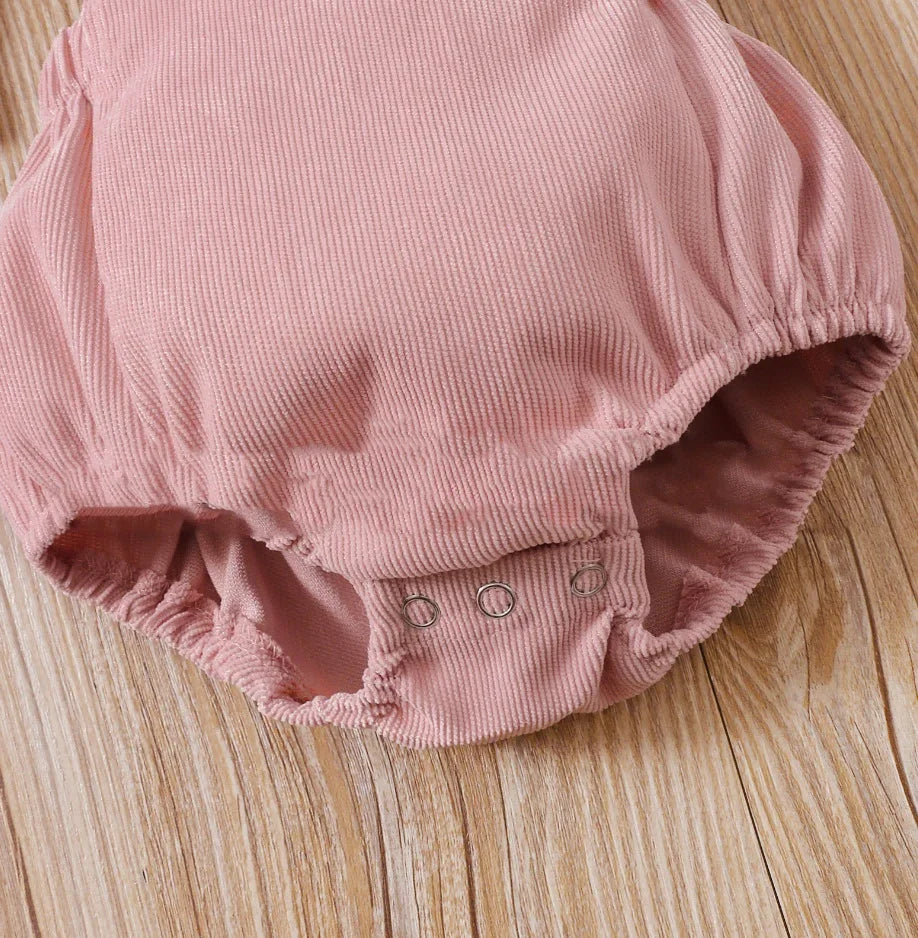 Pink ribbed baby romper with snap buttons on wooden surface