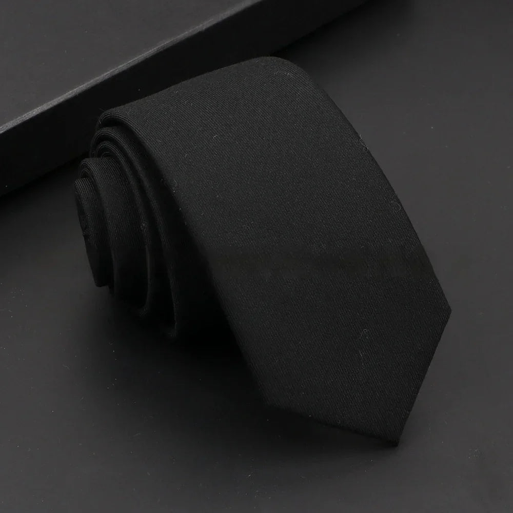 rolled solid black necktie on a dark surface with a black box in the background