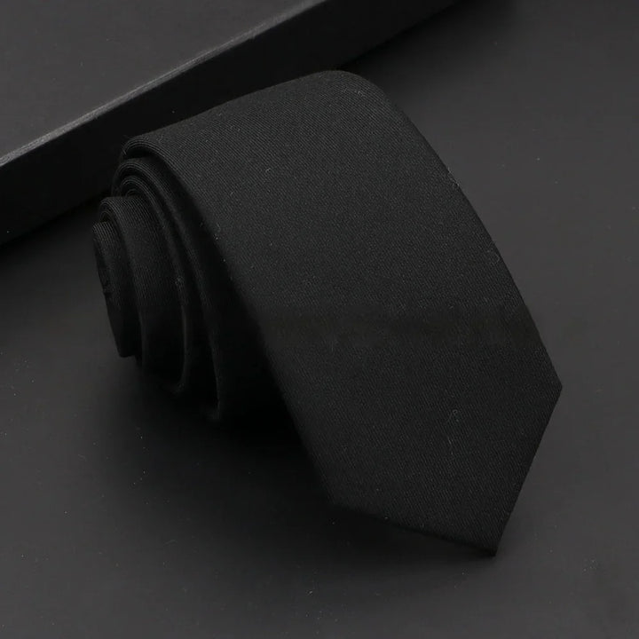 rolled solid black necktie on a dark surface with a black box in the background