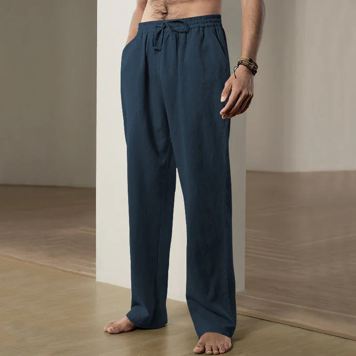 Men's navy blue drawstring linen pants worn barefoot in minimalist indoor setting