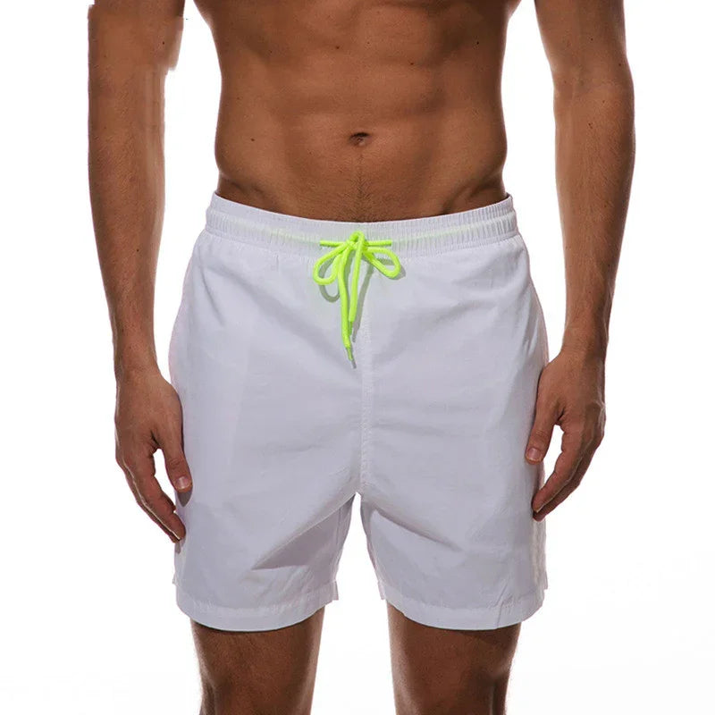 Athletic man wearing white swim shorts with neon green drawstring on white background