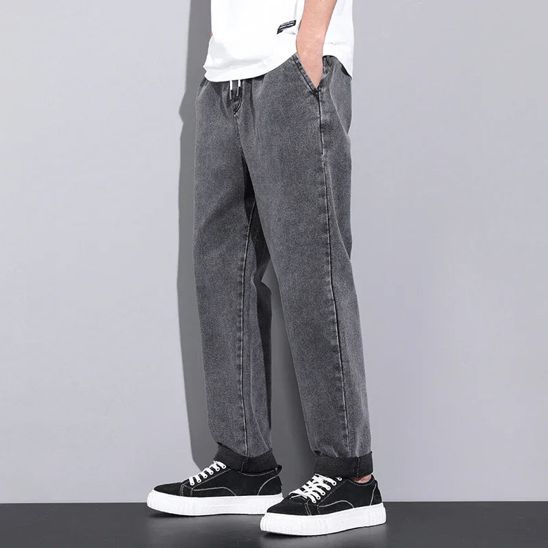 Casual men's grey washed jeans with black sneakers and white soles, hands in pockets