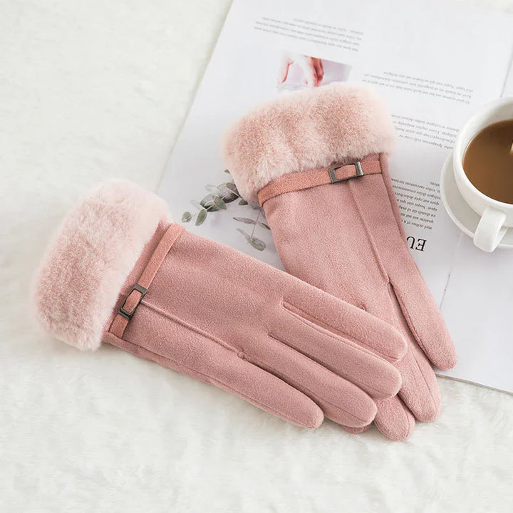 Pair of pink warm gloves with faux fur cuffs and small buckle detail on white surface with coffee cup