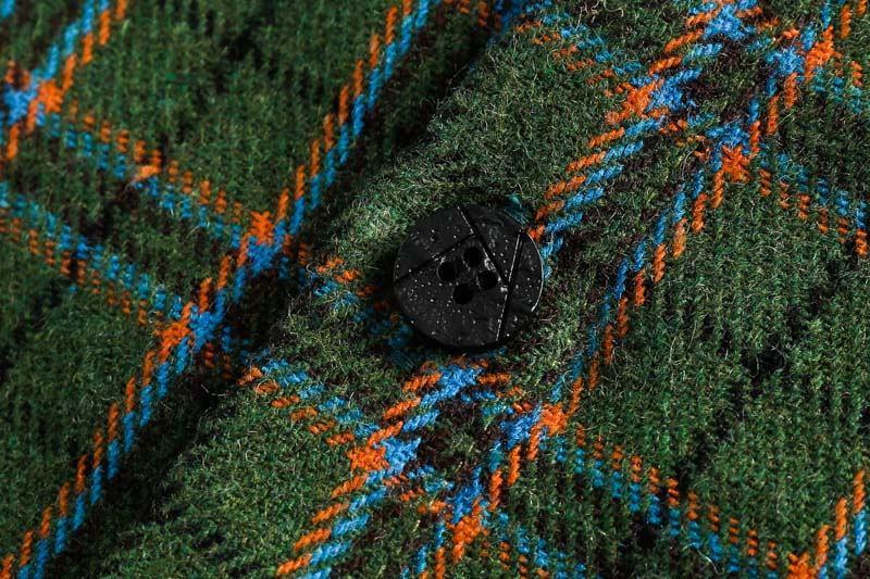 Close-up of green wool fabric with blue and orange plaid pattern featuring a textured black button