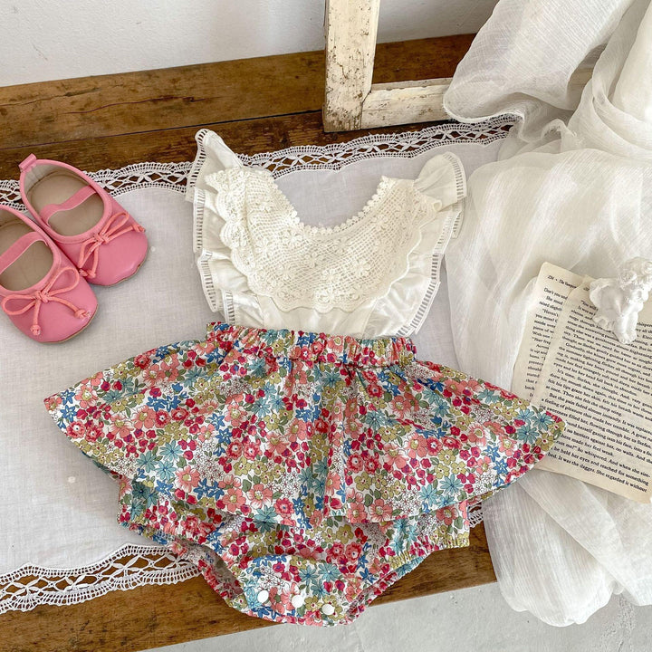 Baby floral romper with lace top and pink shoes on wooden surface with white fabric