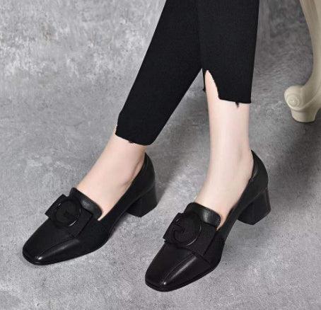 Black block heel shoes with buckle detail worn with black ankle pants on gray floor
